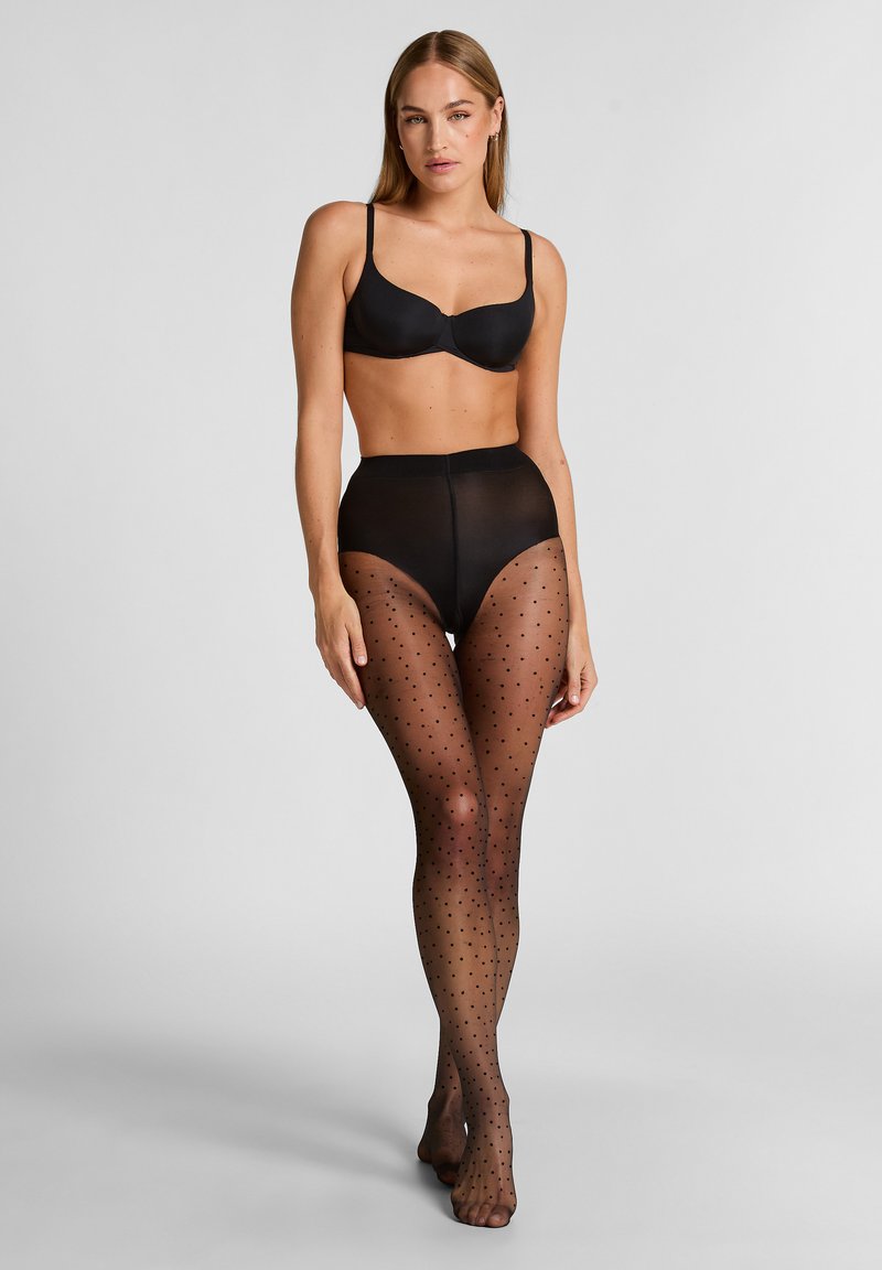 Zwarte bh met een gladde afwerking en verstelbare bandjes, gecombineerd met hoge doorschijnende zwarte panty’s met kleine stippen.