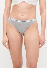 Tanga in misto cotone grigio con elastico bianco recante il logo 'Calvin Klein'. Texture liscia, design a vita bassa, copertura minima.