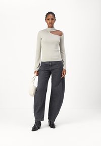 Haut gris clair à manches longues avec une découpe sur l'épaule gauche, associé à un jean noir taille haute à jambes larges et un sac à main blanc.