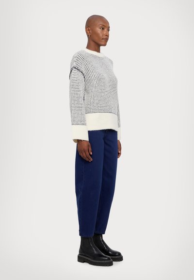 Knitted gray and white sweater with a crew neck and textured pattern, paired with loose dark blue pants and black ankle boots.