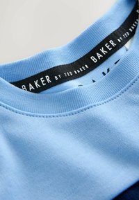 Világoskék pamut póló kerek nyakkivágással, bordás szegéllyel és egy fekete, fehér betűs „BAKER by TED BAKER” feliratú címkével.