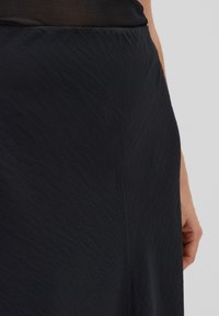 Schwarzer Rock aus strukturiertem Stoff, mit fließendem Design und glattem Bund. Die Oberfläche weist subtile Falten auf.