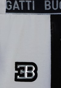 Nahaufnahme von schwarz-weißer Stoff mit silbernem EB-Logo und dem Text "GATTI BU" auf einem schwarzen Streifen oben.