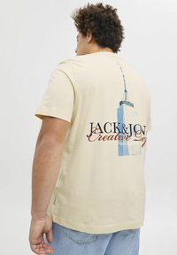 Heled kollane lühikeste varrukatega T-särk, mille seljal on pilvelõhkuja graafika ja tumehallis ning punases tekst "JACK & JON". Puuvillane materjal.