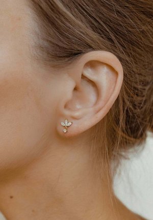 Goldene Ohrringe mit floraler Gestaltung, die mehrere klare Edelsteine aufweisen. Die Ohrringe haben eine zarte und filigrane Form und sind am Ohr eines Modells angeordnet.