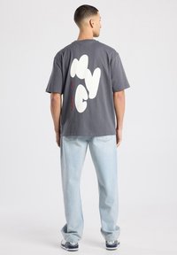 Grijs katoenen T-shirt met een grote witte "NYC" afbeelding op de achterkant, gecombineerd met lichtblauwe spijkerbroek en marineblauwe schoenen. Eenvoudig, comfortabel ontwerp.