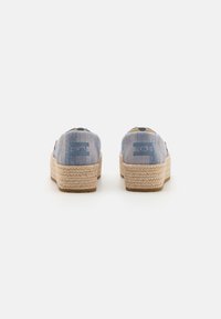 Szövetből készült, kék slip-on cipők természetes juta platform talppal. A hátoldalán a logó részletezése és egy texturált felület látható.