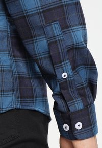 Niebieska i czarna koszula w kratkę z długimi rękawami, z białymi guzikami i miękką fakturą materiału. Wzór składa się z wyraźnych kwadratów.