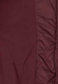 Burgundska odjeća s mekanim, teksturiranim flisom s jedne strane i glatkim, sjajnim materijalom s druge strane. Uključuje detalje šivanja duž šavova.