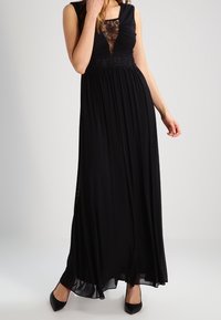 Svart maxiklänning med en åtsittande överdel som har spetsdetaljer, insvängd midja och flödande kjol. Tyget är lätt och mjukt.
