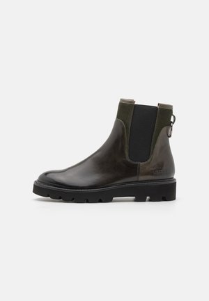 Bottines en cuir marron foncé avec des panneaux élastiques latéraux, des accents verts, une languette et une semelle en caoutchouc noir épaisse. Fini poli.