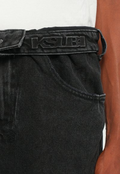 Los jeans de mezclilla negra cuentan con una cinturilla texturizada con logotipo en relieve. Tienen bolsillos laterales y un ajuste relajado con costuras visibles.