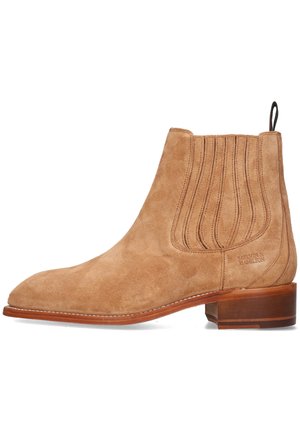 Stivale Chelsea in suede beige con punta arrotondata, pannelli laterali elasticizzati e un piccolo tacco in pelle. Presenta cuciture verticali e branding inciso.