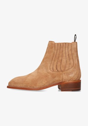 Stivale Chelsea in suede beige con punta arrotondata, pannelli laterali elasticizzati e un piccolo tacco in pelle. Presenta cuciture verticali e branding inciso.