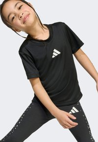 Black athletic t-shirt with short sleeves featuring a white adidas logo. Matte texture leggings with a shiny dotted pattern on the side.