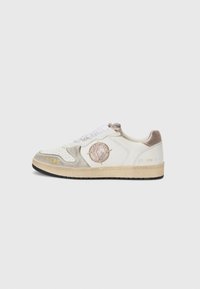 Sneaker bianco con accenti in suede grigio, patch rotondo con logo, testo dorato e lacci bianchi. Presenta una suola in gomma testurizzata e una parte superiore in pelle liscia.