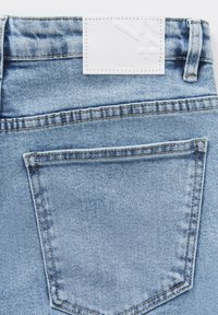 Light blue denim jeans featuring a white leather label at the waistband and a back pocket with contrasting stitching.