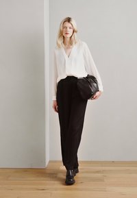 Blusa bianca con scollo a V, pantaloni neri a gamba larga e una borsa nera a tracolla. Le scarpe sono nere e chunky. Design semplice e minimalista.