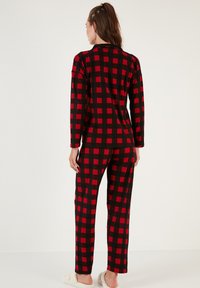 Conjunto de pijama a cuadros rojos y negros hecho de tela suave, con mangas largas y pantalones, que tiene un corte holgado y una textura lisa.