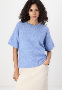 Sweater de malha azul clara com mangas curtas, decote redondo e um corte descontraído; usado sobre uma saia de cor creme com um design em A.