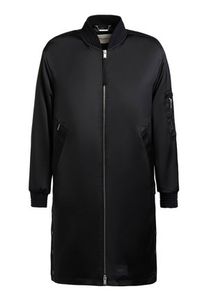 Hosszú fekete bomber dzseki elöl cipzárral, cipzáras oldalzsebekkel, bordázott mandzsettákkal és a bal ujján cipzáras zsebbel.