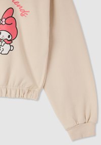 Manica di felpa beige con polsino arricciato, con un personaggio dei cartoni animati con un cappello rosa e la scritta "Il mio dolce amico" in rosa.