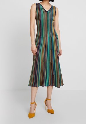 Robe midi sans manches à col en V avec des rayures verticales en bleu sarcelle, jaune, violet et noir, associée à des talons à brides à la cheville jaune moutarde.