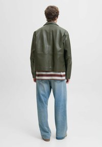 Chaqueta de cuero verde oliva con un corte corto, vista desde la parte de atrás. Combinada con una camisa a rayas y unos pantalones vaqueros holgados de color azul claro.