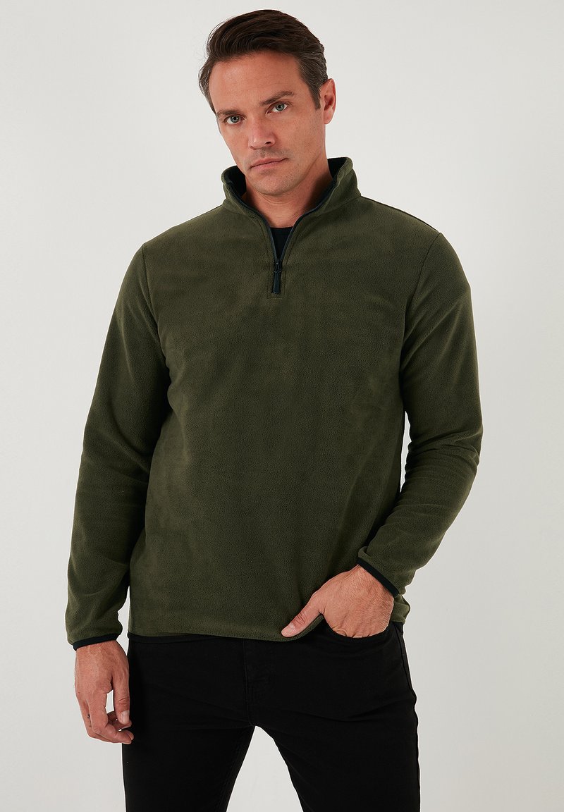 Olivengrøn fleece-pullover med kvart lynlås, lange ærmer og kontrasterende sort kant ved ærmerne. Blødt, struktureret stof er synligt.