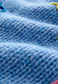 Gestructureerde blauwe gebreide stof met verschillende tinten, met opstaande steken en kleurrijke geborduurde accenten die door elkaar zijn verspreid.