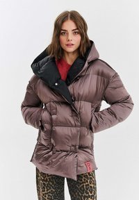 Puchowa, nieregularnie pikowana kurtka w kolorze fioletowym z czarnym kapturem, z zapięciem na guziki i dwiema przednimi kieszeniami. Ozdobiona czerwoną metką.