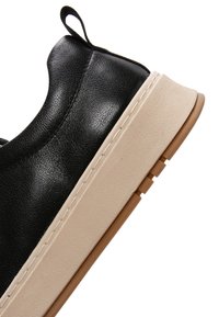 Niskie czarne skórzane trampki z beżową grubą podeszwą i brązowym bieżnikiem, z czarną pętlą do zakładania na pięcie.