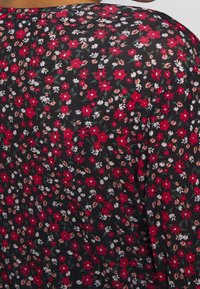 Tela negra con un denso patrón floral en pequeños tonos rojos, blancos y beiges, acompañado de hojas verdes, en una prenda de vestir.