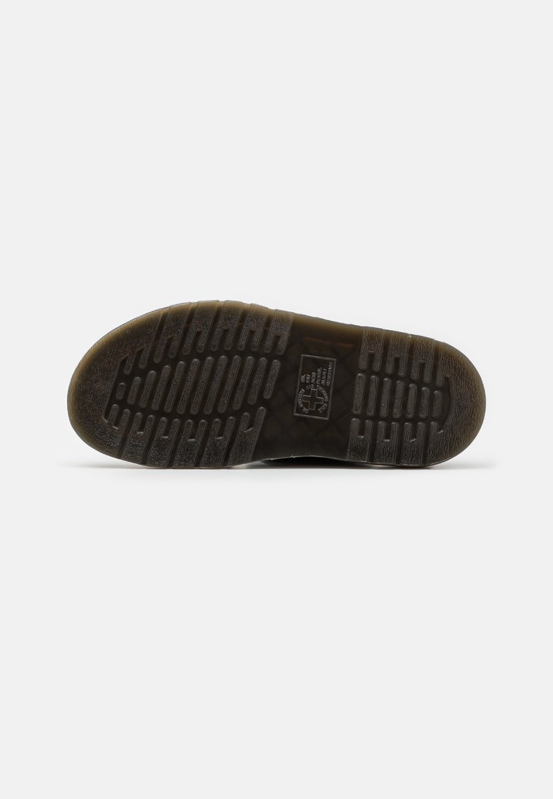Black rubber sneaker sole with textured grooves, circular heel, and detailed tread pattern. Labels visible near the center.