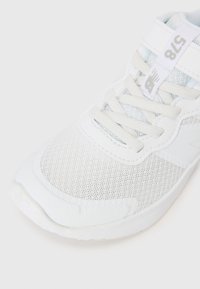 Baskets de sport blanches avec une tige en mesh, des superpositions texturées, des lacets plats et une étiquette logo sur la languette. Semelle lisse avec un profil minimal.