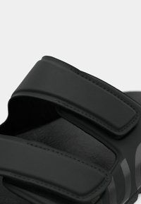 Sorte sandaler med to brede, teksturerte stropper med borrelås. Myk, matt finish med en konturert såle og sømløst design.