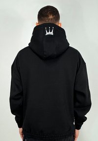 Schwarzes Hoodie mit einer großen Rückentasche, dickem Stoff, verstellbarer Kapuze und einem weißen Kronenlogo, das auf dem Rücken gestickt ist. Einfaches und lässiges Design.