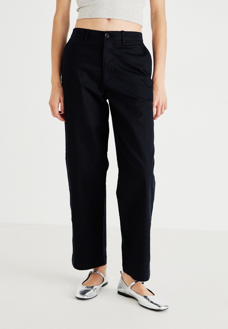Black high-waisted trousers with a straight-leg design, made from a smooth fabric. Features a button closure and side pockets.