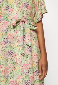 Vestido de estampado floral con una tela suave, mangas cortas, un cinturón en la cintura y botones en una paleta de colores pastel que incluye rosa, morado y verde.