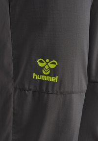 Zwarte sportbroek met een gladde textuur, voorzien van een felgroen Hummel-logo en bijenembleem op de linker bovenbeen.