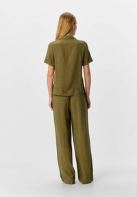 Ensemble deux pièces vert olive comprenant une chemise à col à manches courtes et un pantalon large, tous deux en tissu lisse et texturé.