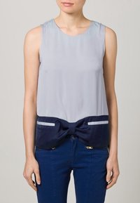 Ärmlöst linne med en ljusgrå övre del och en marinblå nedre del med en knutdekoration. Slät tyg med kontrasterande ränder.