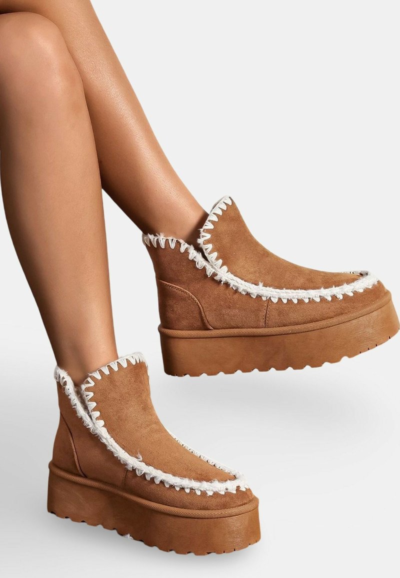 Bottes de cheville en suède marron avec un détail de couture en zigzag blanc le long du bord, dotées d'une semelle plateforme épaisse et d'un design à bout rond.
