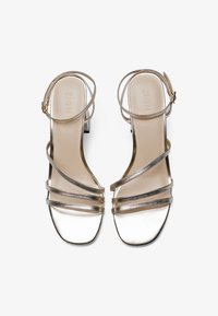 Strapiga högklackade sandaler i metalliskt silver med två tunna vristband och en fyrkantig tådesign. Slät yta och låg blockklack.