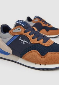 Zapatillas que presentan una mezcla de malla azul marino y ante marrón, con acentos beige y un talón azul. Logo visible en el lado y en la lengüeta.
