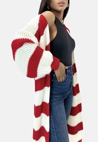 Czerwony i biały sweter na guziki w paski z szerokimi rękawami, noszony na czarnej bluzce bez rękawów i niebieskich, wysokich dżinsach.