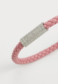 Pulsera de cuero trenzado rosa con un cierre de metal plateado que lleva grabado el logo "GUESS". El diseño es elegante y contemporáneo.