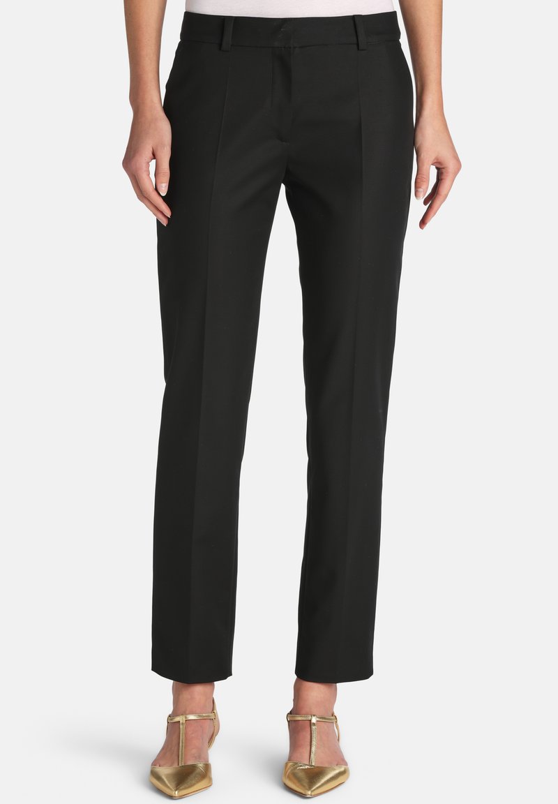 Black tailored straight-leg trousers worn with gold pointed-toe T-strap heels, shown from waist to feet on a white background.