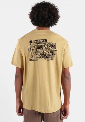 T-shirt à manches courtes de couleur jaune pâle, présentant un graphique noir détaillé d'une scène de motel imprimée dans le dos, avec une coupe décontractée et une texture douce.