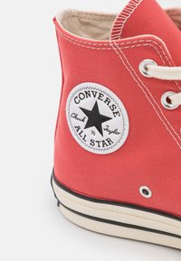 Tenis alto de tela vermelha com um patch do logotipo de estrela preta, atacadores brancos e sola de borracha bege com contorno preto.